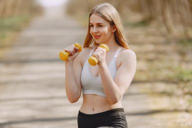 Fit woman lifting dumbbells on a sunny day, embracing a healthy outdoor workout.